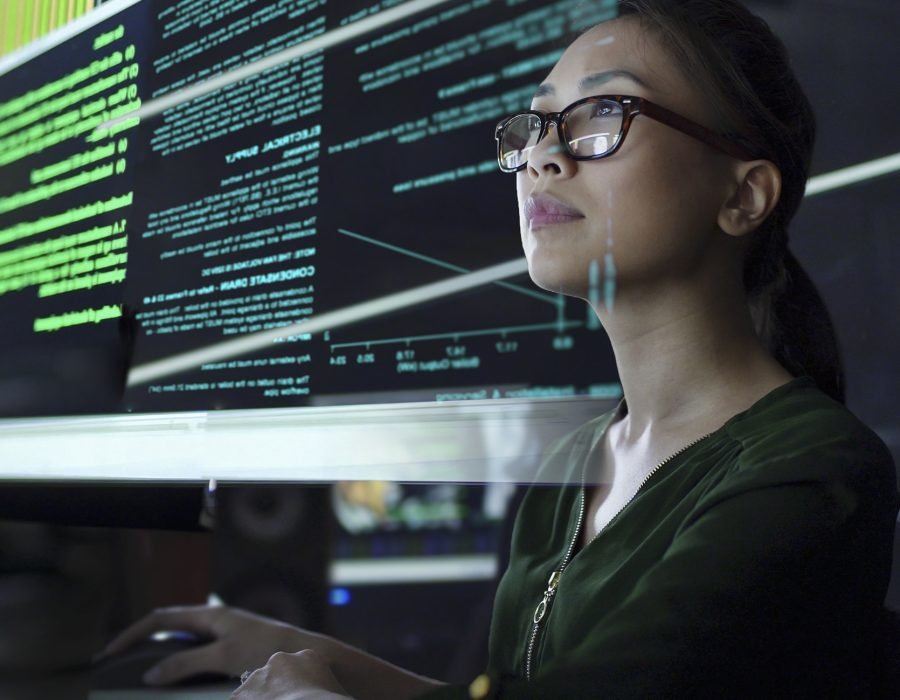 Stock photo of a young Asian woman looking at see through data whilst seated in a dark office